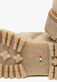 Botte beige clair avec une semelle texturée robuste, présentant un profil imposant, des coutures renforcées et un emblème du drapeau italien sur la semelle extérieure.