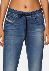 Blue denim jogger pants with an elastic waistband, black drawstring, front pockets, and faded texture details.