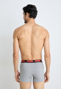 Szürke boxer alsónadrág, fekete derékkal, amelyen piros "PUMA" felirat található. A dizájn szorosan illeszkedik, és a comb középső hosszúságáig ér.
