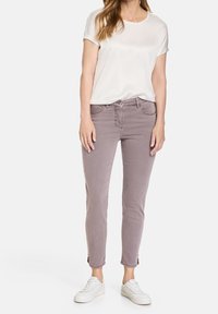Vaqueros ajustados de un gris claro con un ligero desgaste y puños de longitud tobillo, combinados con una blusa crema de manga corta y zapatillas blancas.