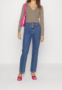 Braunes, geripptes Langarmshirt mit V-Ausschnitt und Perlendetails, kombiniert mit hoch taillierten blauen Straight-Leg-Jeans und pinken Sandalen mit Blockabsatz.