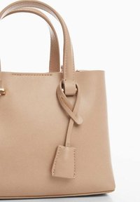 Borsa in pelle beige con due manici superiori, dettaglio a nodo sulla tracolla e un'etichetta rettangolare. Texture liscia e design minimalista.