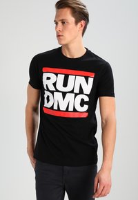 Černé bavlněné tričko s odvážným bílým potiskem "RUN DMC" s červenými akcenty. Krátké rukávy a kulatý výstřih.