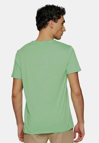 T-shirt vert à manches courtes en tissu lisse, présentant un col rond classique et une coupe décontractée. Aucune motif ou graphique visible.