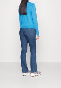 Modrý svetr, krátký střih s pružnými manžetami; tmavě modré bootcut džíny; šedé sportovní boty s růžovými detaily; dlouhé rovné vlasy.