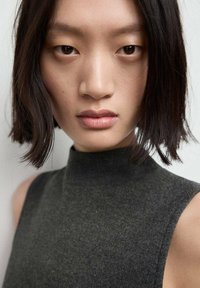 Ingrandimento di una persona con capelli neri lisci e una maglia a collo alto grigio scuro. La trama del tessuto è morbida e opaca con dettagli minimi.