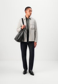 Giacca grigia chiara, polo verde scuro, pantaloni di denim scuro, scarpe di pelle nere e una borsa a spalla di pelle nera. Design semplice con accentuazioni minime.