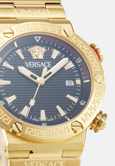 Montre Versace dorée avec un cadran noir texturé, logo de lion, motif de clé grecque sur la lunette et index lumineux ; elle dispose d'un affichage de la date.