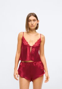 Rød sateng loungewear-sett som inkluderer en camiskjorte med blonder og sløyfedetaljer, kombinert med matchende shorts prydet med blonder.