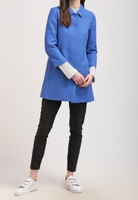 Blue textured coat with a collar, long sleeves, and a straight cut, paired with black slim pants and white sneakers.