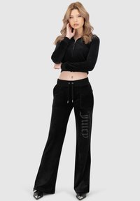 Schwarzes Velours-Zweiteiler-Set: Kurz gepolsterte Zip-Jacke mit langen Ärmeln, schwarze Jogginghosen mit Zugband und mit Strass "Juicy"-Detail am Bein.