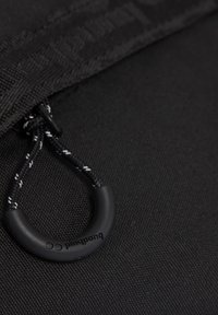 Fermoar negru cu snur împletit și mânere din cauciuc cu marcă, pe o suprafață de țesătură neagră texturată.