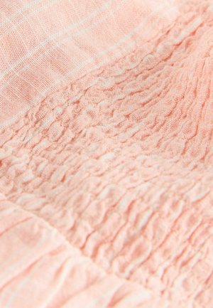 Weicher rosa Stoff mit gesammelter, geraffter Textur, die eine zerknitterte, elastische Oberfläche und ein sichtbares Webmuster in Nahaufnahme zeigt.