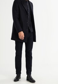 Abrigo de lana azul marino con solapas de muesca, diseño de un solo botón y cierre con botones, combinado con vaqueros oscuros y botines de cuero negro.