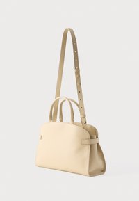 Μπεζ δερμάτινη τσάντα χειρός με δύο πάνω λαβές και ρυθμιζόμενο μακρύ λουράκι, σε απλό λευκό φόντο.