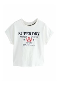 Bílá bavlněná tričko s krátkými rolovanými rukávy, na kterém je nápis "SUPERDRY" v námořnické modři a červené barvě, spolu se starožitným znakem.