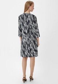 Kurzarmkleid im navy und weißen abstrakten Muster; verfügt über eine lockere Passform, einen runden Halsausschnitt und endet über dem Knie. Schwarze Absätze Sandalen.