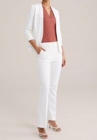 Valkoinen bleiseri, joka on kerrostettu ruosteenvärisen, pitsireunuksellisen topin päälle, yhdistetty valkoisiin housuihin ja valkoisiin remmikkäisiin korkokenkiin. Yksinkertainen, räätälöity malli.