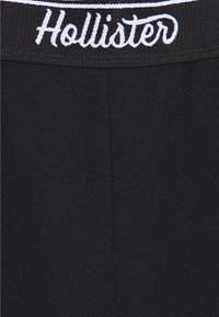 Černé bavlněné legíny s širokým černým pasem, na kterém je vyšívaný text "Hollister" v bílé barvě. Hladká textura s mírným protažením.