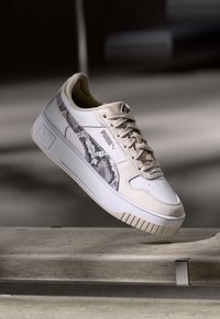 Sneaker w kolorze kremowym z teksturowanym akcentem w wężowy wzór po boku, z gładką skórzaną cholewką, sznurowanym zapięciem i grubą gumową podeszwą.