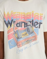 Λευκό βαμβακερό T-shirt με γραφική εκτύπωση ενός κασετόφωνα και ακουστικών. Τα χρώματα περιλαμβάνουν μπλε, κίτρινο, ροζ και μαύρο κείμενο.