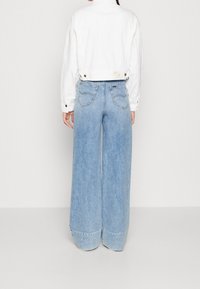 Giacca bianca corta con bottoni a pressione abbinata a jeans denim azzurri a gamba larga con tasche posteriori e orlo rifinito.