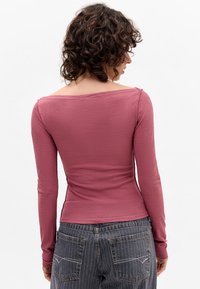 Langarm, aansluitend top in stoffige rozenkleur, met een brede halslijn en zachte textuur, gecombineerd met gestreepte, hooggetailleerde jeans.