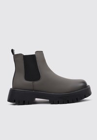 Botas Chelsea de goma grises con suela negra gruesa, con paneles laterales elásticos y una lengüeta para facilitar el calzado. Acabado liso, diseño moderno.