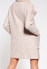 Cappotto in misto lana beige chiaro con un morbido colletto in pelliccia, maniche lunghe, tasche laterali e una silhouette rilassata, caratterizzato da una finitura testurizzata.