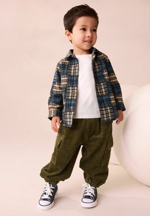 Plaid button-up shirt in blue, brown, and green; white tee; olive corduroy pants; navy sneakers with white laces; relaxed fit.
