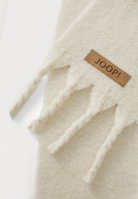 Cremefarvet uldhalstørklæde med teksturerede ender og et rektangulært brunt lædermærke prægede med "JOOP!"