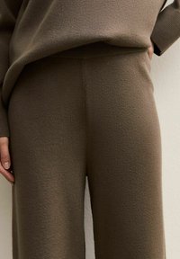 Pantalons en tricot marron avec une texture douce, présentant une coupe décontractée et une taille haute. Le tissu semble chaud et confortable.