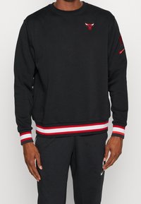 Sudadera negra con puños y dobladillo a rayas rojas y blancas. Cuenta con un pequeño logo de toro rojo en el pecho y un logo de Nike en la manga. Material de mezcla de algodón.