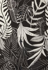 Lyhythihainen paita, jossa on musta tausta ja valkoisia kasvitieteellisiä lehtikuvioita, napit ja sileä kangas. 