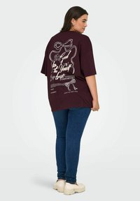 Overdimensjonert burgunder t-skjorte med hvit grafisk tekst og sløyfedesign bak. Kombinert med blå smale jeans og off-white plattform sko.