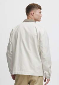 Crème katoenen jas met een tan kleurige kraag, knoopmanchetten en een rechte snit. De achteraanblik benadrukt het minimalistische ontwerp.