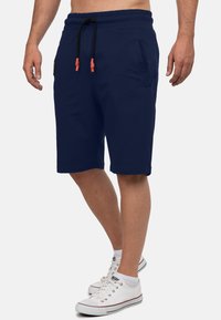 Marineblauwe shorts van zachte stof, met een elastische tailleband, zwart trekkoord met oranje uiteinden en zijzakken.
