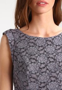 Robe en dentelle avec un tissu gris texturé à motifs floraux, encolure ronde et manches courtes, mettant l'accent sur des détails délicats.