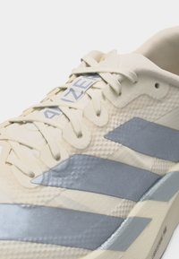 Μπεζ και γκρι αθλητικό παπούτσι με κορδόνια, με υφή στην επάνω επιφάνεια, επενδεδυμένο γιακά και την επιγραφή "AZER" στο ετικετάκι της γλώσσας.