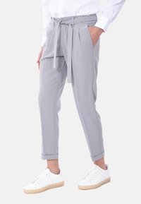 Pantaloni tapered grigio chiaro realizzati in tessuto liscio, con vita alta con cintura, pieghe e orli arrotolati, abbinati a sneakers bianche.
