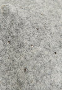 Tela de felpa gris con una textura peluda, que presenta tachuelas metálicas dispersas por la superficie para darle un detalle adicional.