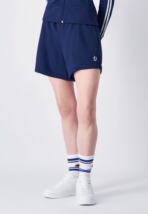 Marineblaue Sportshorts mit einem Kordelzugbund, aus glattem Material gefertigt, kombiniert mit weißen Sneakern und gestreiften Socken.