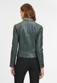 Giacca di pelle verde con una texture liscia, design aderente e cuciture sulle spalle; presenta una piccola patch con logo sulla manica.