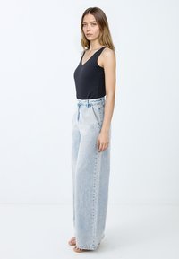 Body nero senza maniche abbinato a jeans a vita alta in denim blu chiaro con gambe ampie, caratterizzati da orli sfrangiati e una texture di denim lavato chiaro.