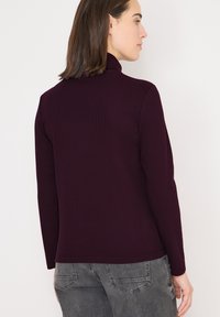 Burgundowy, prążkowany top z długim rękawem i wysokim kołnierzem, o dopasowanym kroju i gładkiej fakturze, w połączeniu z szarymi dżinsami.