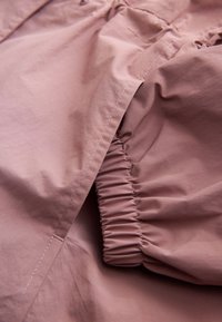Gros plan d’un tissu rose poudré avec un poignet élastique et des coutures visibles sur la manche d’un vêtement.