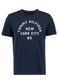 Námořnická modrá pánská bavlněná tričko s designem kulatého výstřihu, na kterém je bíle potištěný text: "TOMMY HILFIGER NEW YORK CITY 85" v oblouku.
