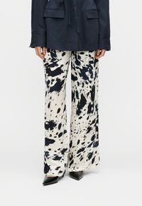 Παντελόνια με φαρδιά γραμμή σε εκρού βάση με μαύρα σχέδια σαν πιτσιλιές. Μαλακό ύφασμα με απαλή υφή. Συνδυασμένα με μαύρες μυτερές γόβες.