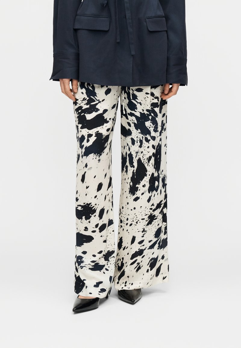 Παντελόνια με φαρδιά γραμμή σε εκρού βάση με μαύρα σχέδια σαν πιτσιλιές. Μαλακό ύφασμα με απαλή υφή. Συνδυασμένα με μαύρες μυτερές γόβες.