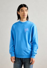 Lichtblauwe sweatshirt van katoen, met een ronde hals, geribbelde manchetten en een roze logo op de linker voorkant. Gemaakt met denim jeans.